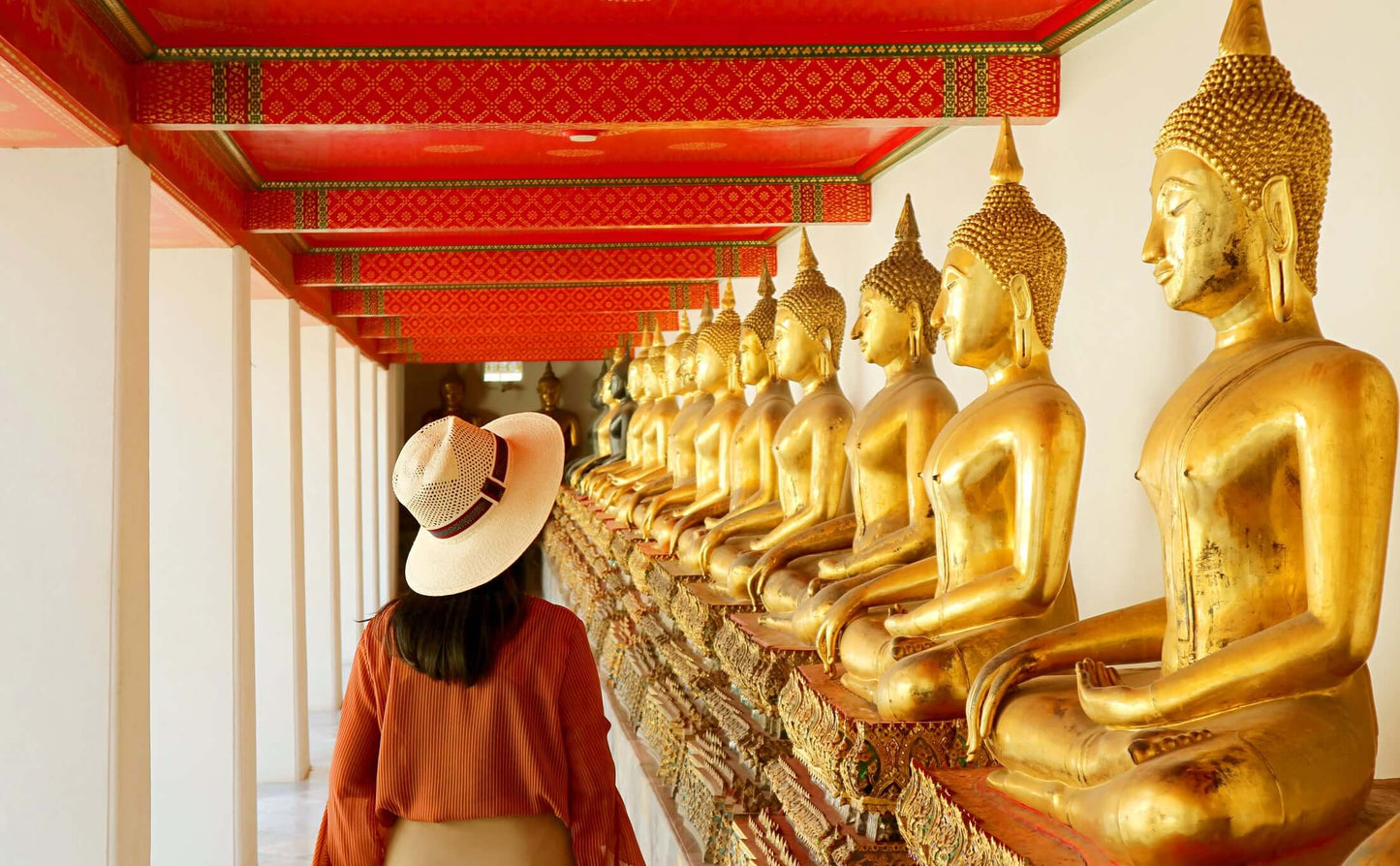 Visitor admiring golden Buddha statues in a temple corridor in Bangkok, showcasing rich Thai architecture and spirituality.