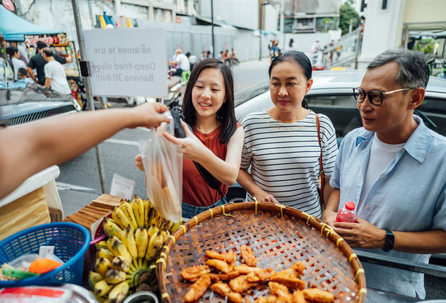 Visitors enjoying street food at a bustling Bangkok market, sampling snacks and local delicacies.