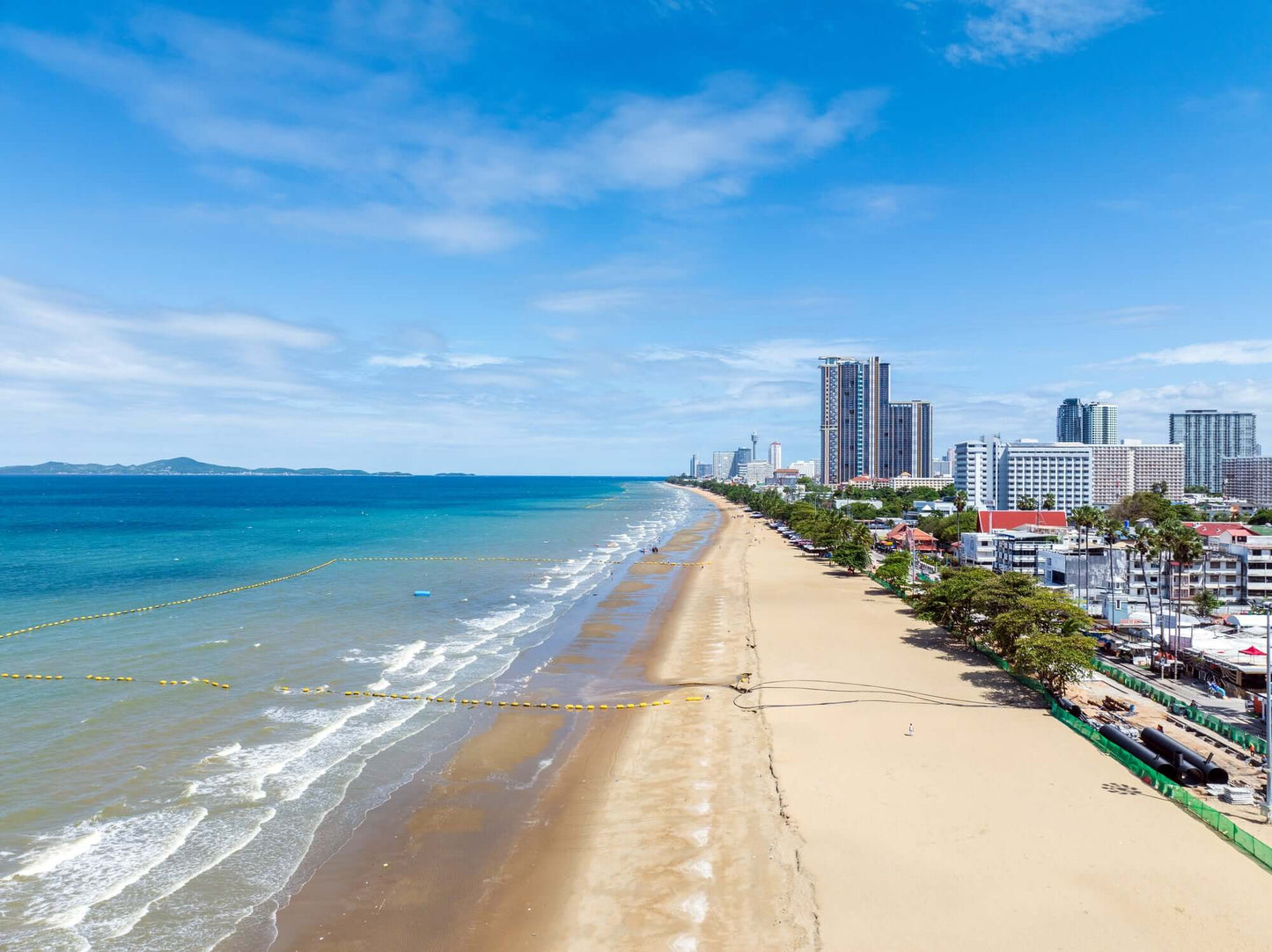 A stunning view of Pattaya Beach featuring golden sands, blue waters, and city skyline under a clear sky.