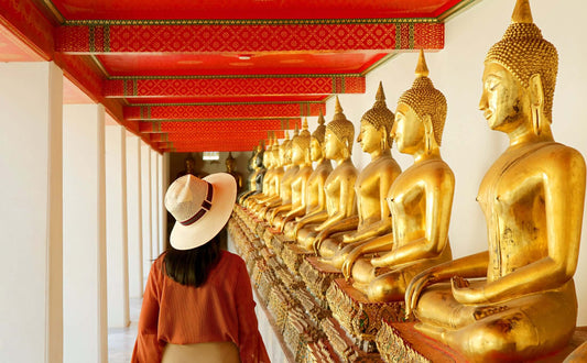 Visitor admiring golden Buddha statues in a temple corridor in Bangkok, showcasing rich Thai architecture and spirituality.