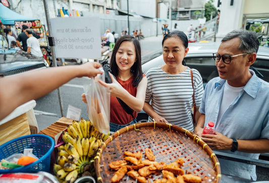 Visitors enjoying street food at a bustling Bangkok market, sampling snacks and local delicacies.